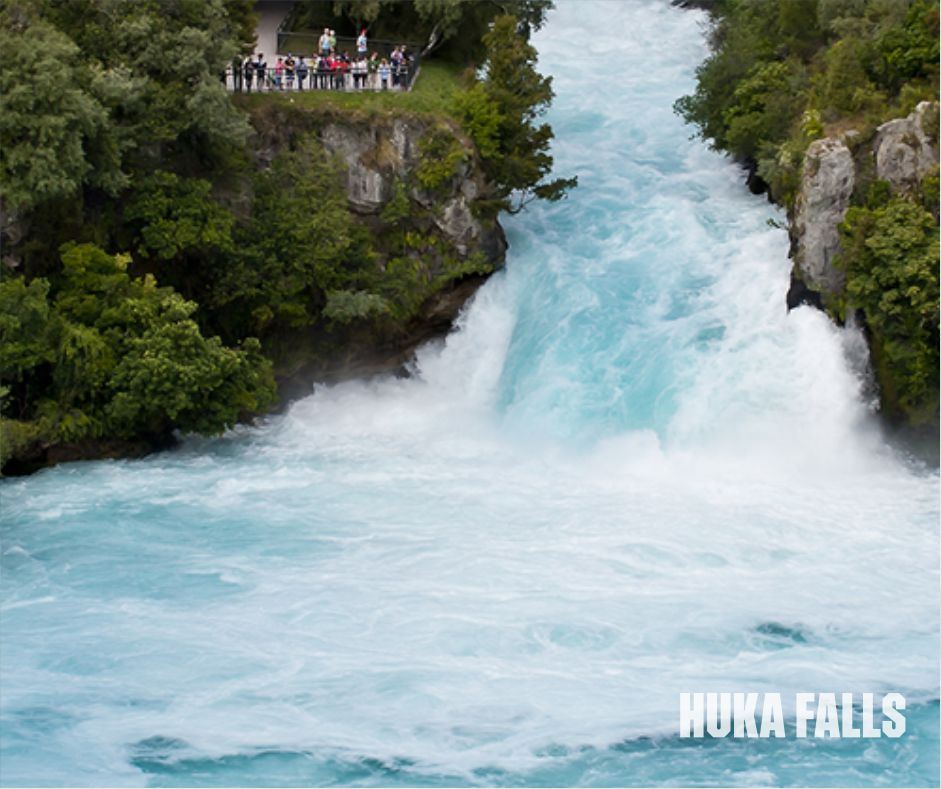 Huka Falls, New Zealand, features vibrant blue water rushing over a rocky ledge, framed by dense vegetation.
